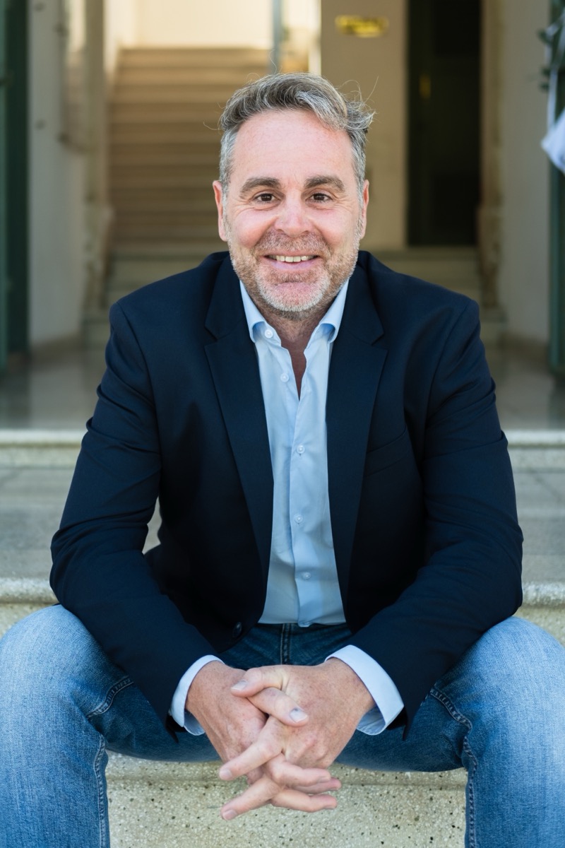 Joris Bryon, seated on stone steps in a navy blazer